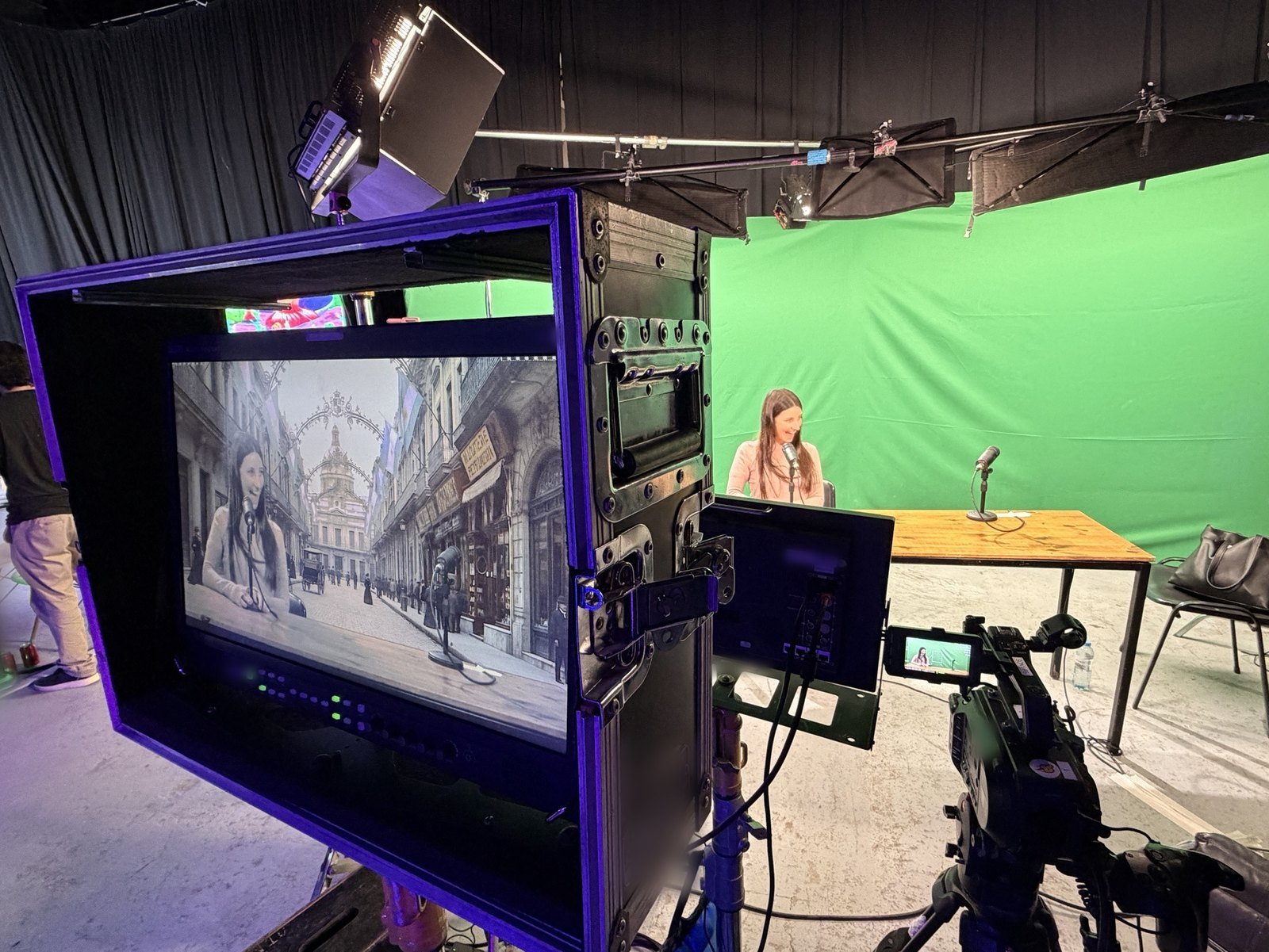 An actress at a table on a green screen stage while the monitor shows her already in a Buenos Aires street of 1910